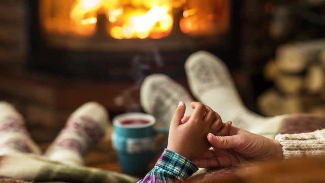 Warm atmosphere near the fireplace. Female and children's feet in woolen socks, steam rises from a hot drink.