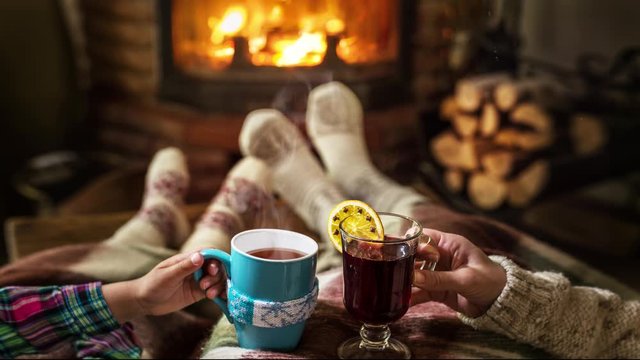 Warm atmosphere near the fireplace. In women's and child hands in a warm sweater, steam rises from a hot drinks.