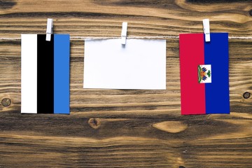 Hanging flags of Estonia and Haiti attached to rope with clothes pins with copy space on white note paper on wooden background.Diplomatic relations between countries.