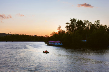 A man in a boat floats on the river at sunset. The athlete in the boat is not far from the picturesque shore in the evening. Beautiful sunset, a walk along the river.