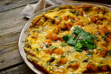 Omelet in a white beautiful plate. Omelet with yellow tomato, pepper and parsley leaves. Appetizing breakfast. Wooden light background. Egg shells, textiles.