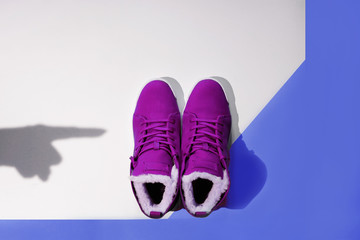 A pair of female purple winter sneakers stands on a blue and white background with a shadow from a female hand pointing to buy, flatlay, copyspace, top view, minimal, art