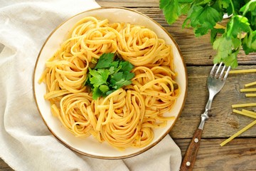 Pasta in a beautiful white plate. Pasta on a light wooden background. Spaghetti with parsley leaves. Macaroni, parsley, lemon, sweet yellow pepper.