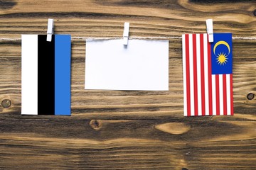 Hanging flags of Estonia and Malaysia attached to rope with clothes pins with copy space on white note paper on wooden background.Diplomatic relations between countries.