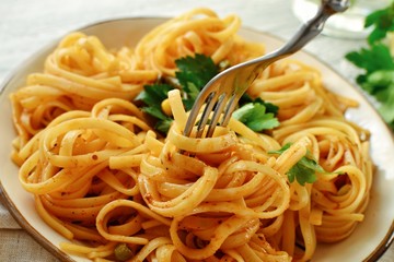 Pasta in a beautiful white plate. Pasta on a light wooden background. Spaghetti with parsley leaves. Macaroni, parsley, lemon, sweet yellow pepper. Spaghetti on a fork.