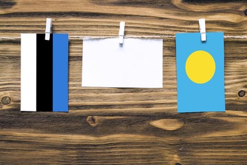 Hanging flags of Estonia and Palau attached to rope with clothes pins with copy space on white note paper on wooden background.Diplomatic relations between countries.