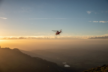 Obraz na płótnie Canvas Helikopter fliegt über Berge in den Sonnenuntergang 