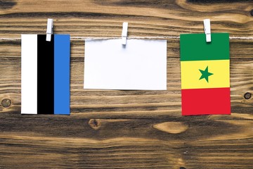 Hanging flags of Estonia and Senegal attached to rope with clothes pins with copy space on white note paper on wooden background.Diplomatic relations between countries.