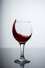 splashes of red wine in a glass on a black glossy glass on a white background