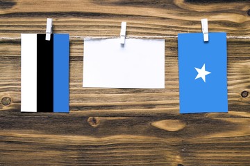 Hanging flags of Estonia and Somalia attached to rope with clothes pins with copy space on white note paper on wooden background.Diplomatic relations between countries.