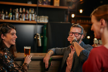 Group of friends drinking beer, chatting and having good time at pub. Night out.