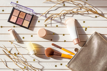 New Year's set of girl makeup cosmetics. Women accessories in silver cosmetic bag -  eyeshadows, face brushes, creams and lotions on Christmas white wooden background with golden stars.