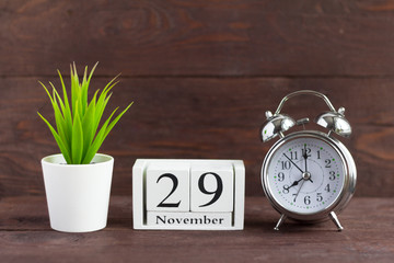 November 29 on a wooden calendar next to an alarm clock on a wooden background, the calendar date of the last autumn month