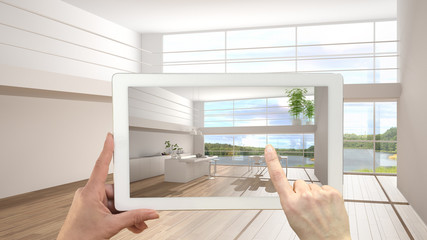 Fototapeta na wymiar Augmented reality concept. Hand holding tablet with AR application used to simulate furniture and design products in empty interior with parquet floor, modern white kitchen