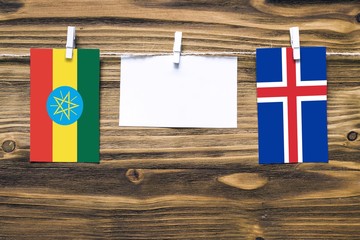 Hanging flags of Ethiopia and Iceland attached to rope with clothes pins with copy space on white note paper on wooden background.Diplomatic relations between countries.