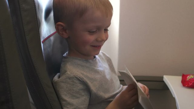 Close-up portrait of a little boy on a plane, he is vomits and he is holding a special package for vomiting. The kid's vomits on the plane, he's vomiting. Slow motion.