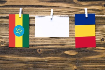 Hanging flags of Ethiopia and Romania attached to rope with clothes pins with copy space on white note paper on wooden background.Diplomatic relations between countries.