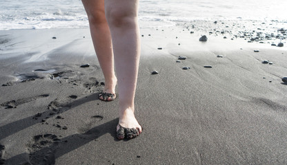 Lady walking on the sand with refreshment wet legs in black sand beach on an island. Sandy Fingers...