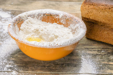 bowl of flour, egg, milk is on a wooden table, next to a loaf of bread. The concept of baking bread.