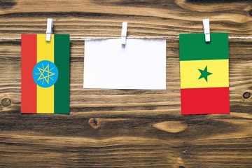 Hanging flags of Ethiopia and Senegal attached to rope with clothes pins with copy space on white note paper on wooden background.Diplomatic relations between countries.