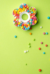 Creative layout of flower shape with colorful candies over green background and place for text