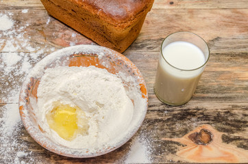 Fresh bread brick on the table closeup. Next is a bowl of flour and egg, a glass of milk.