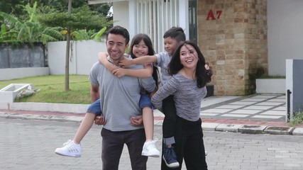 two kids with their parent having fun together in front of their new house. piggyback ride