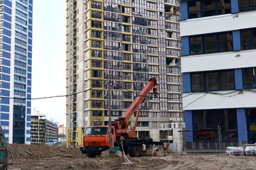 Auto crane at a construction site on the background new residential skyscraper and the construction of a vein of multi-storey buildings. Unloading of cargo and building materials by mobile truck crane