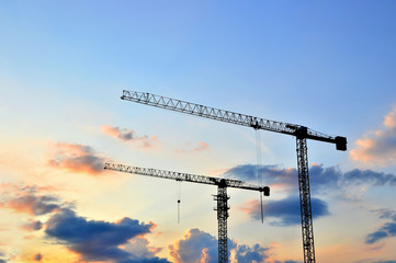 Tower cranes at construction site in the sunset sky background. Renovation program, development,...