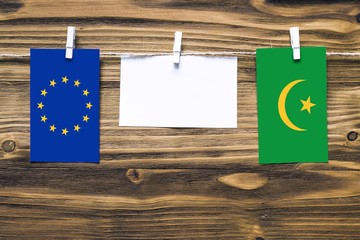Hanging flags of European Union and Mauritania attached to rope with clothes pins with copy space on white note paper on wooden background.Diplomatic relations between countries.