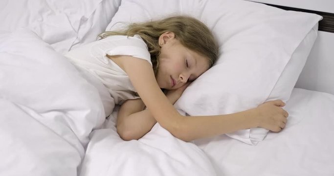 Girl child ten years old with long curly blond hair sleeping in white bed on pillow