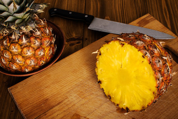 Pineapple and knife sits on a wood chopping board on wooden background.