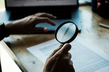 Businessman looking through a magnifying glass to documents. Business assessment and audit....