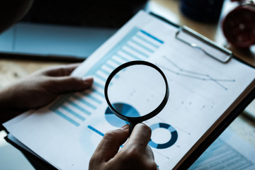 Businessman looking through a magnifying glass to documents. Business assessment and audit....