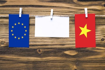 Hanging flags of European Union and Vietnam attached to rope with clothes pins with copy space on white note paper on wooden background.Diplomatic relations between countries.