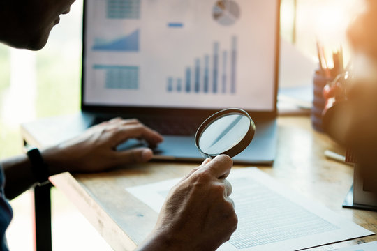 Businessman looking through a magnifying glass to documents. Business assessment and audit. Magnifying glass on a financial report. Concept of search.