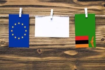 Hanging flags of European Union and Zambia attached to rope with clothes pins with copy space on white note paper on wooden background.Diplomatic relations between countries.