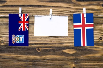 Hanging flags of Falkland Islands and Iceland attached to rope with clothes pins with copy space on white note paper on wooden background.Diplomatic relations between countries.