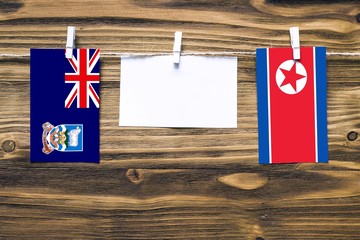 Hanging flags of Falkland Islands and North Korea attached to rope with clothes pins with copy space on white note paper on wooden background.Diplomatic relations between countries.