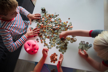 kids count money, boy and girls put coins into piggy bank