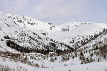 Cottage in a valley surrounded by the Tatra Mountains. Snowy winter weather with clouds. Žiarska valley/ Žiarska cottage. 