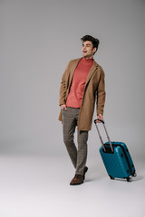 excited man in beige coat walking with suitcase on grey