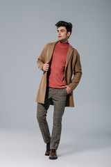 fashionable young man posing in beige coat on grey