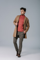 Fototapeta premium fashionable young man posing in beige coat on grey