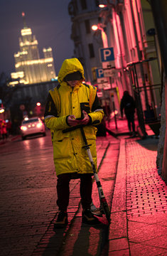 A man in a yellow raincoat stands in a pink night city with a bright building in the background
