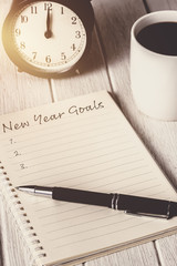 New Year's Goals List written on Notebook with alarm clock, pen, coffee