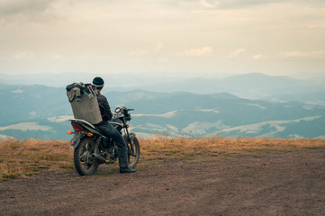 Fototapeta na wymiar Beautiful mountain landscape. A man, a picker of blueberries, on a motorcycle with a box of berries behind him, is preparing to go down the slope of the Carpathian Mountains.