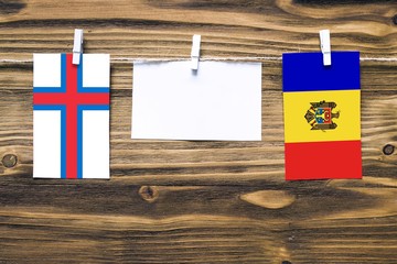 Hanging flags of Faroe Islands and Moldova attached to rope with clothes pins with copy space on white note paper on wooden background.Diplomatic relations between countries.