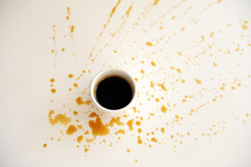 Cup of espresso on a white surface splattered with drops of coffee