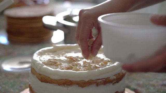 Woman baker puts nuts on a cake with cream.